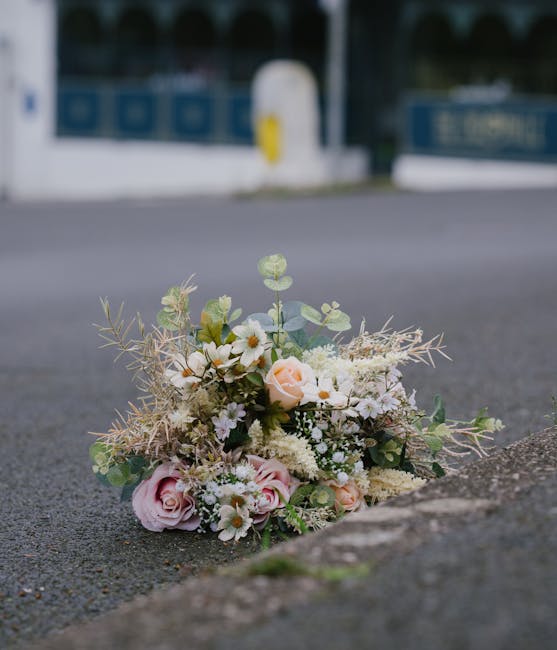 A delicate bouquet of fresh flowers resting on an urban pavement, featuring pale pink roses, white daisies, and soft green eucalyptus leaves, arranged with creamy filler flowers and wispy, dried folia