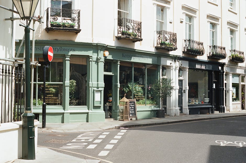 Exterior view of Kensington Flowers, a flower shop with a pastel green facade and large glass windows displaying fresh floral arrangements. The shop is situated on a quiet street near Canonbury Tower 